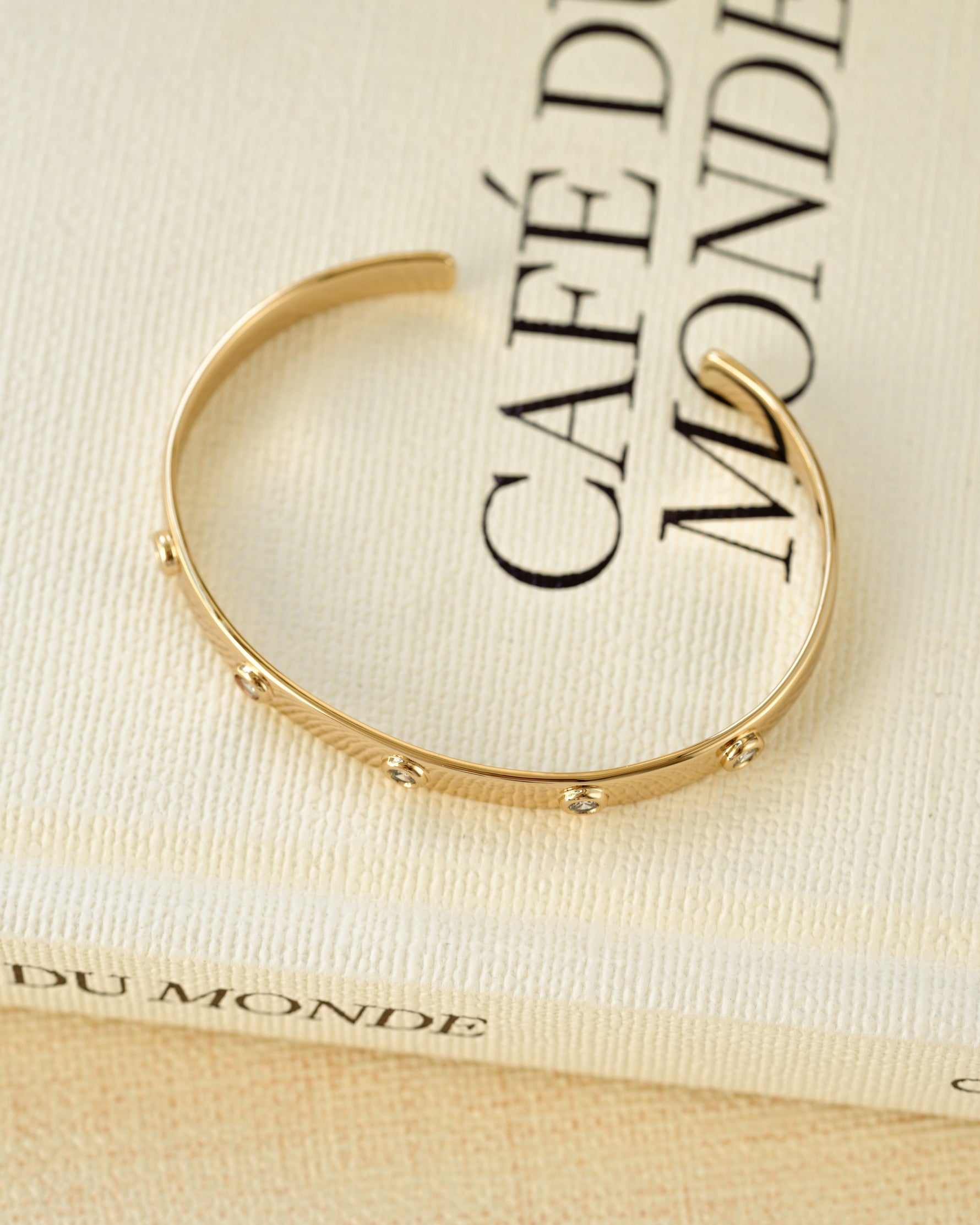 Gold statement jewelry featuring a diamond cuff bracelet on a coffee table book