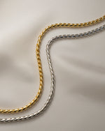 Two snake chain necklaces, one gold chain and one silver chain, on a beige background.