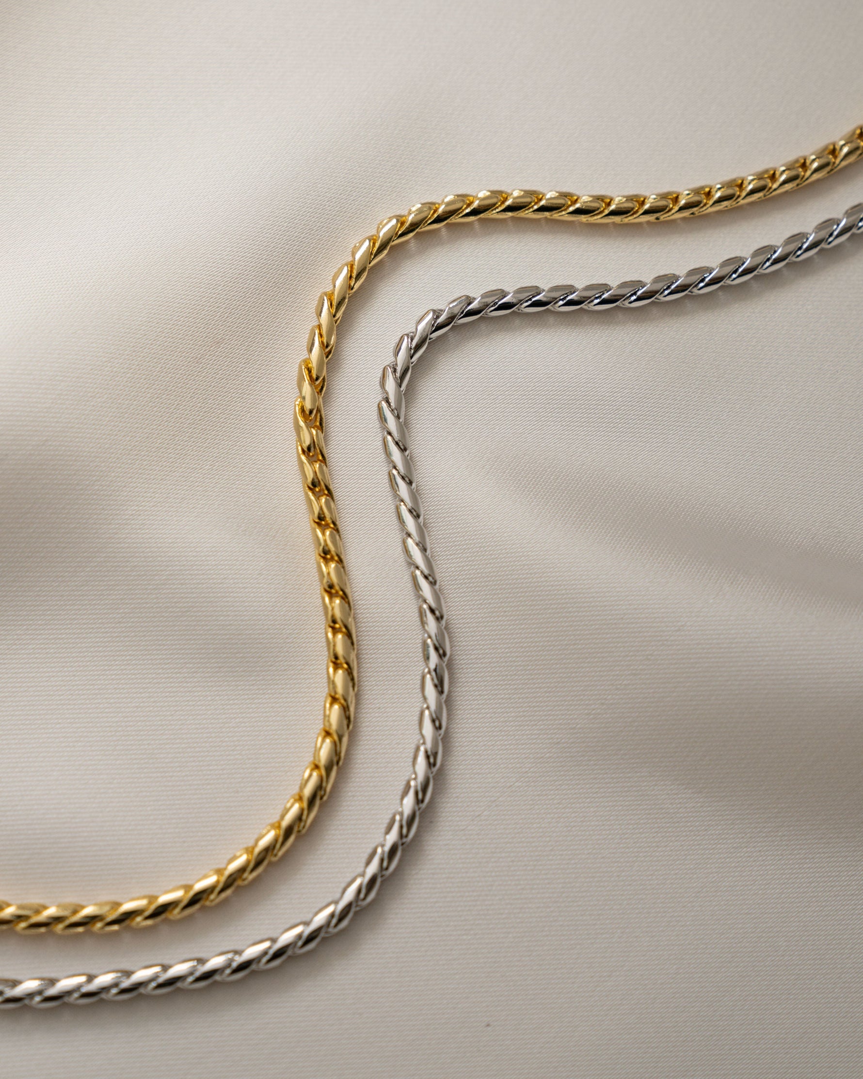 Two snake chain necklaces, one gold chain and one silver chain, on a beige background.