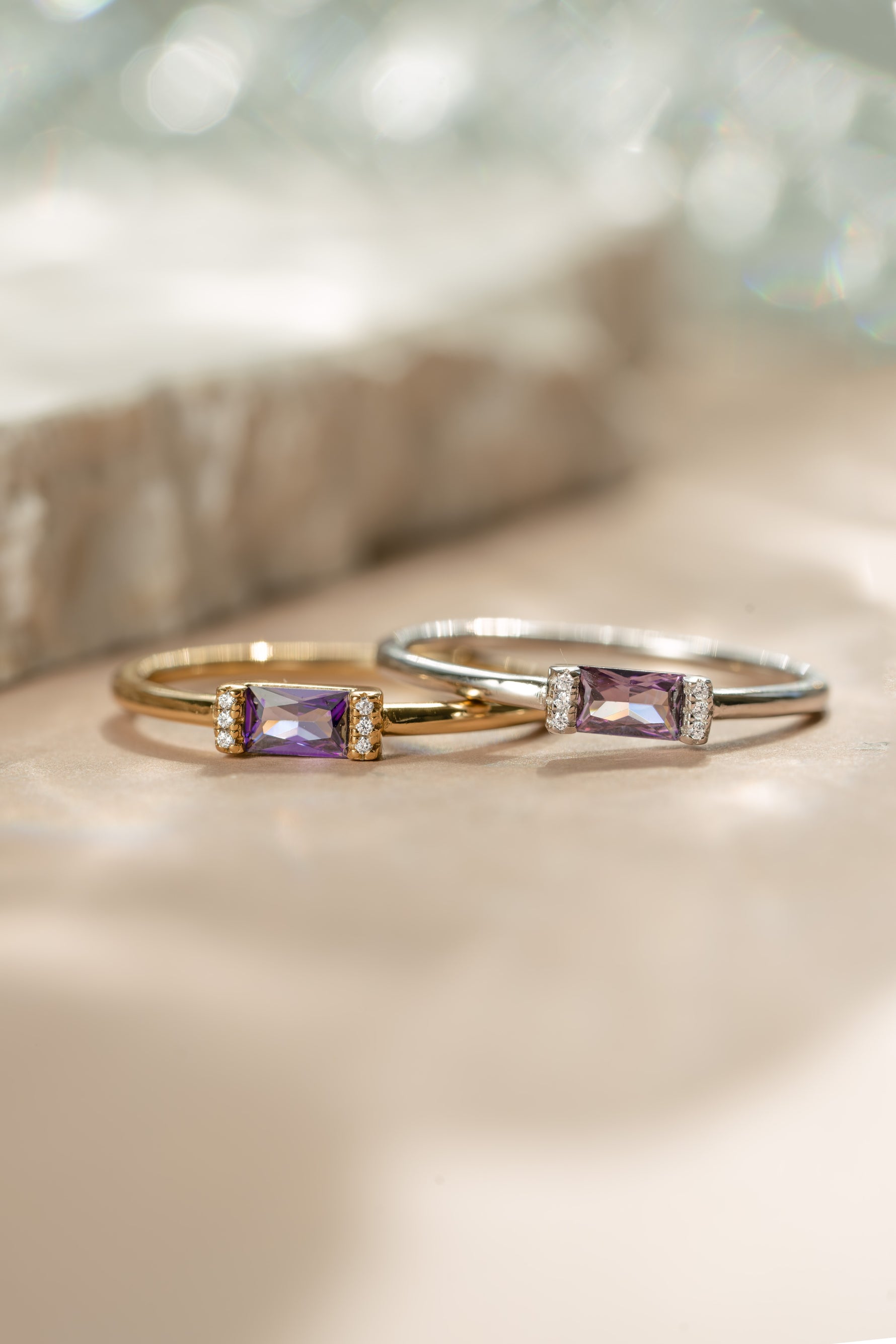 Gold amethyst birthstone ring next to a matching sterling silver baguette ring 