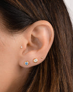 Closeup image of model wearing gold plated earrings featuring a march birthstone earring and a dainty stud earring with a gold ball stud earring