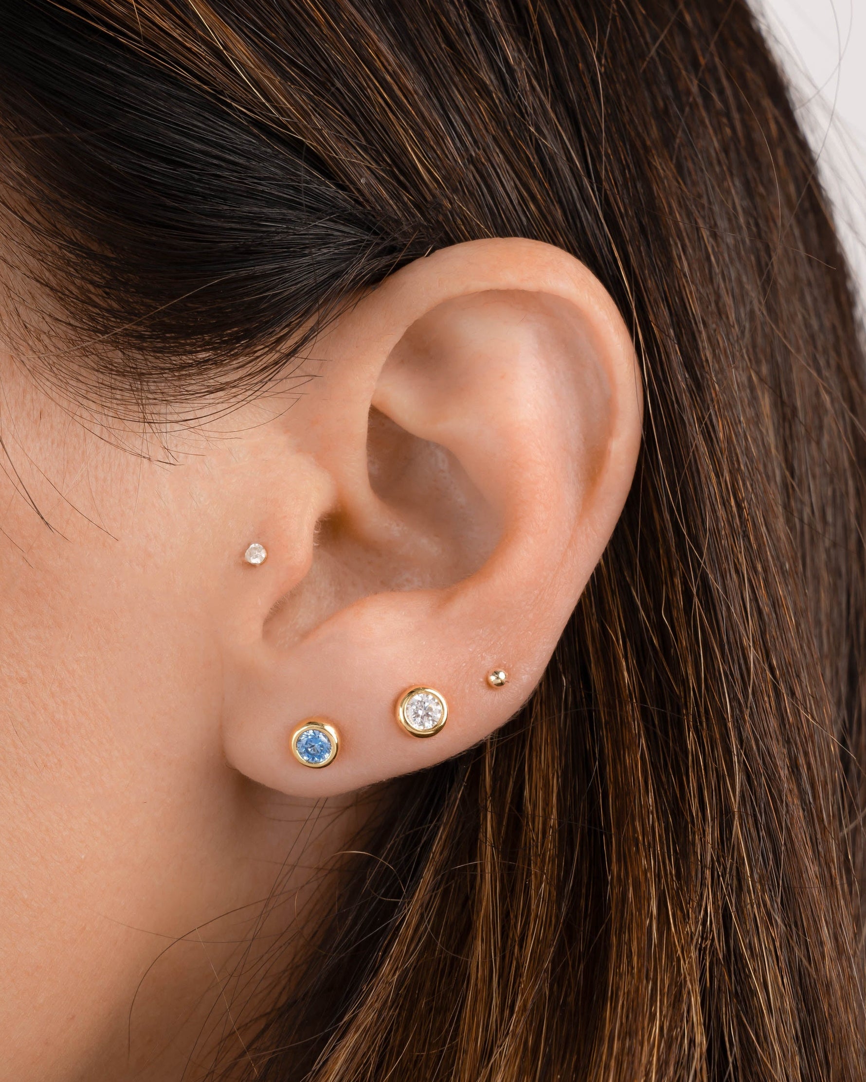 Closeup image of model wearing gold plated earrings featuring a march birthstone earring and a dainty stud earring with a gold ball stud earring