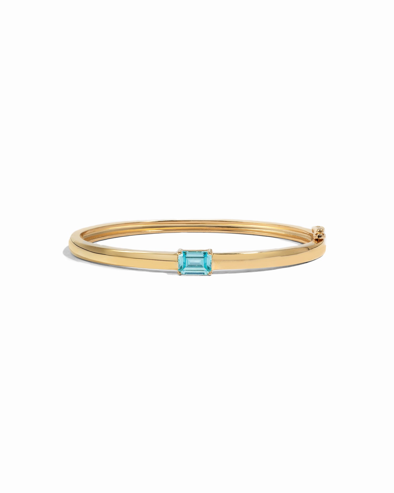 Gold bangle bracelet with a aquamarine gemstone on a white background