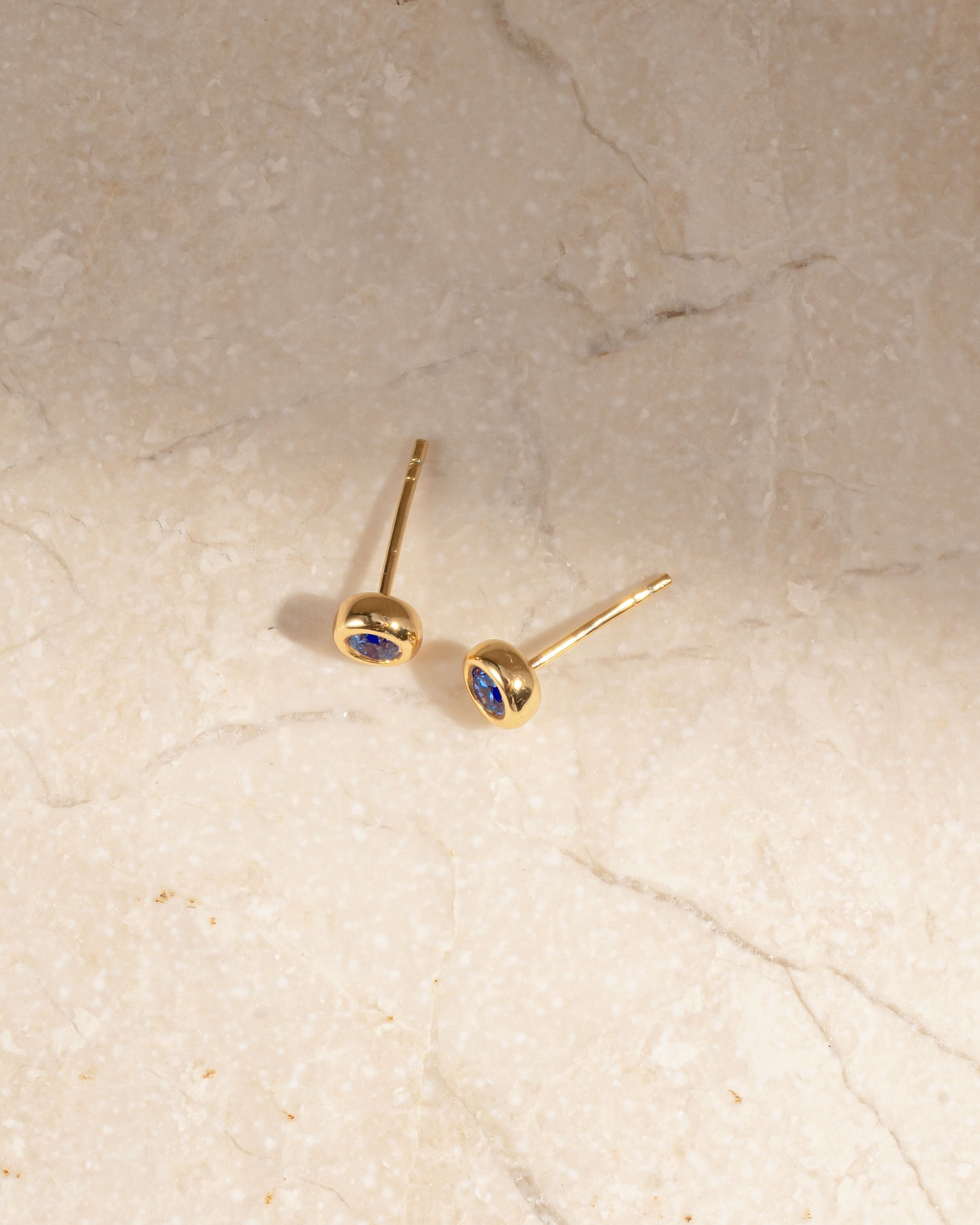 Gold small earrings with the march birthstone on a marble background