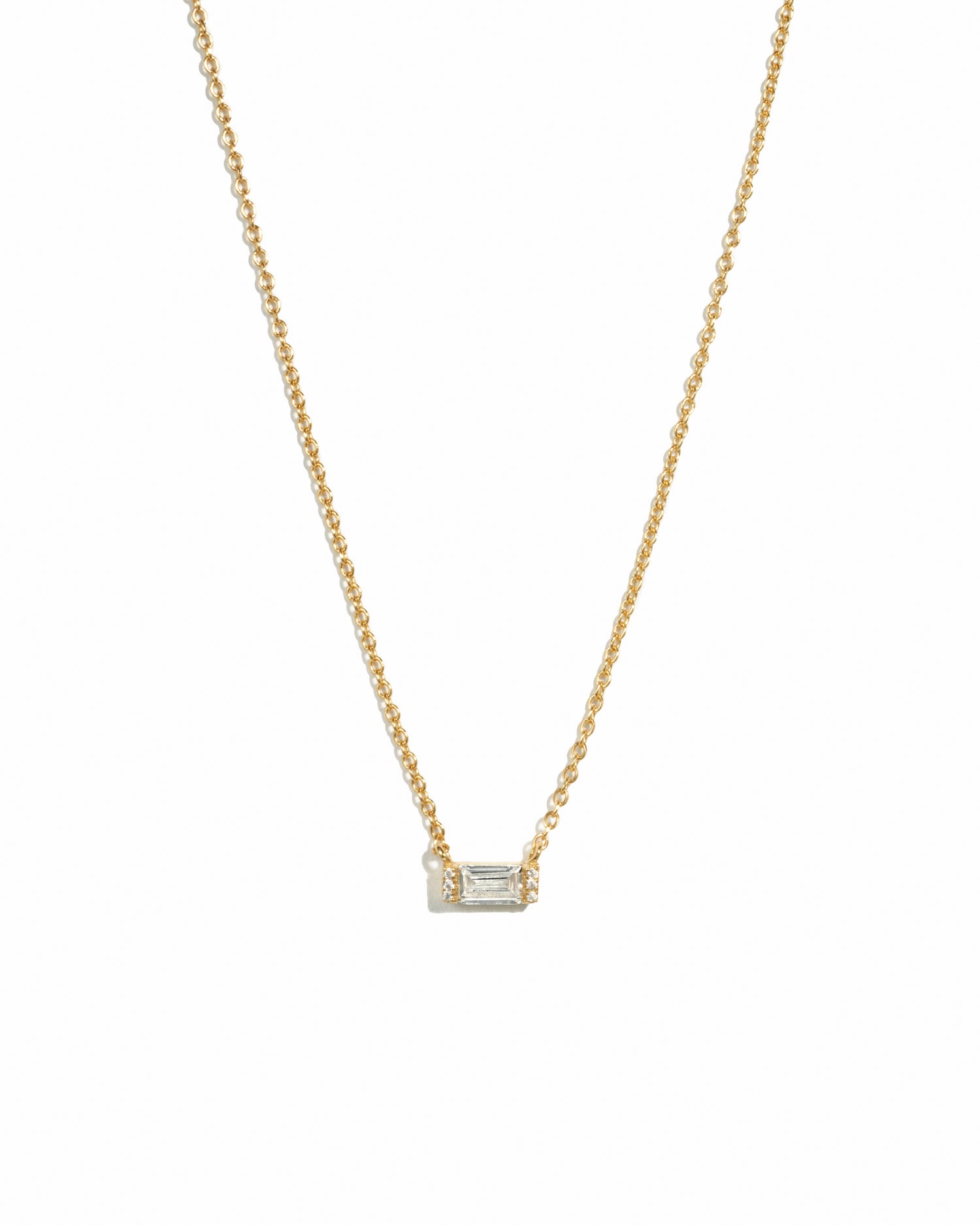 Delicate gold baguette stone necklace on white background.