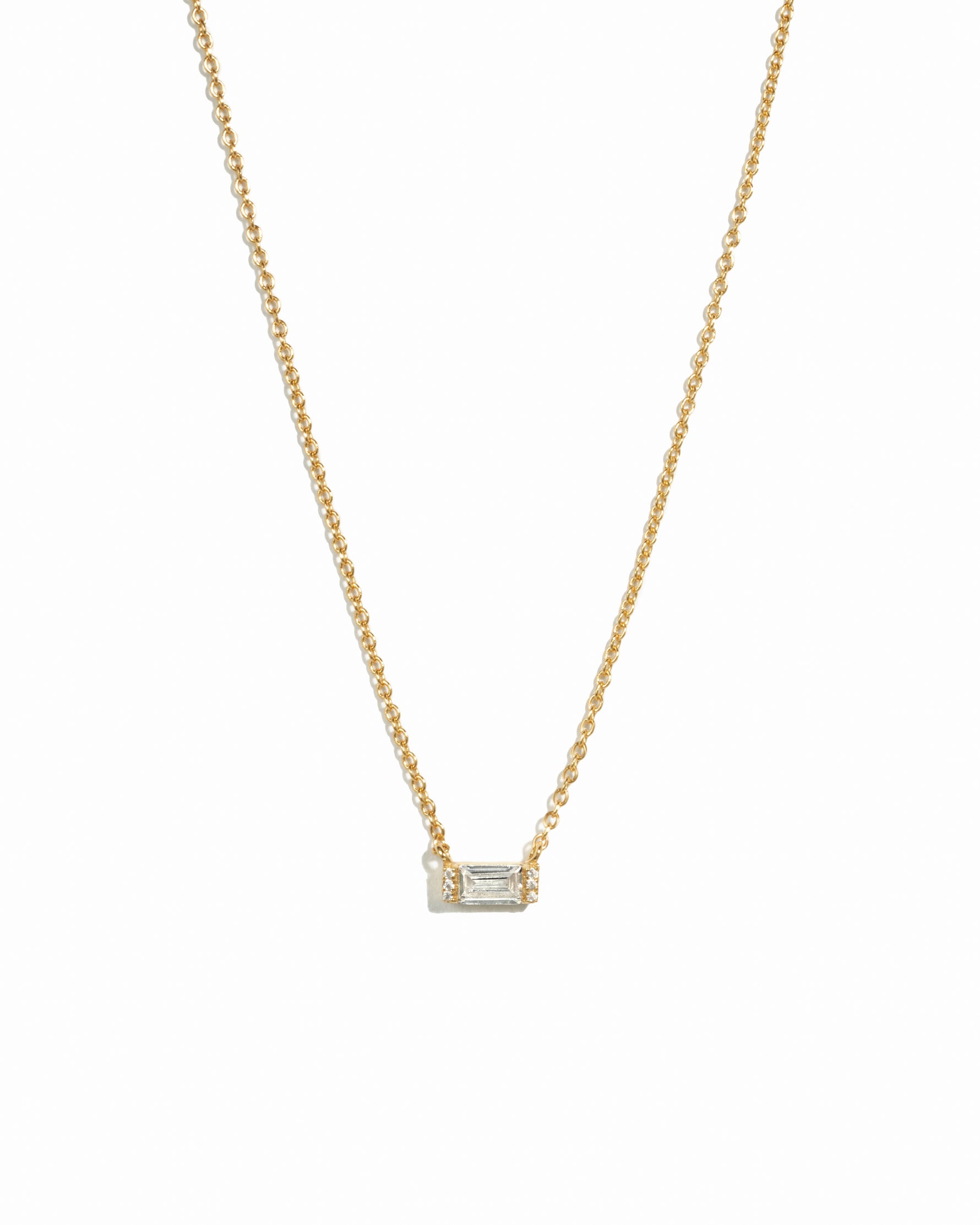 Delicate gold baguette stone necklace on white background.