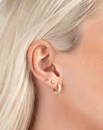 Close-up of a models ear wearing gold hoop earrings, a bezel stud earring, and a ball stud earring