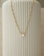gold necklace laying against vase with halo baguette pendant and paperclip chain