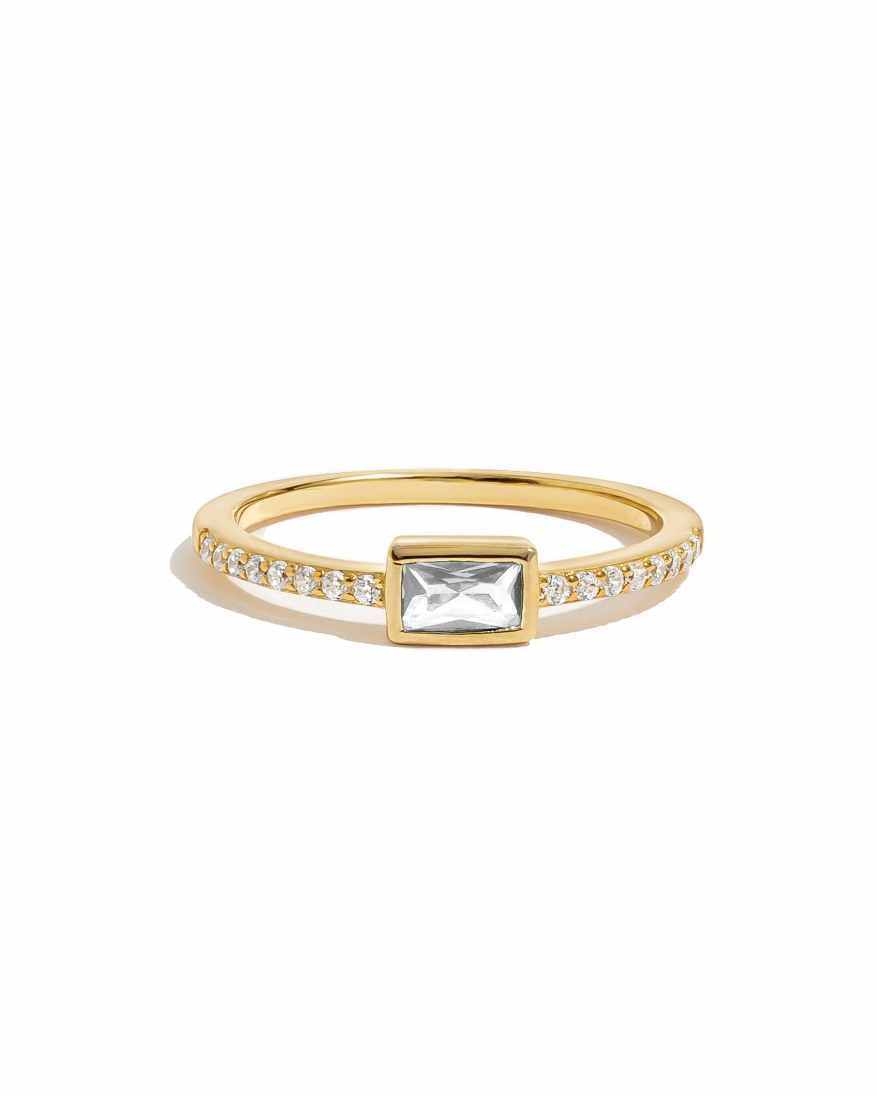 Gold ring with a central gemstone and pave cubic zirconia stones on a white background