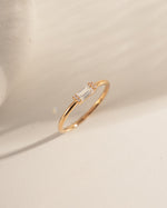 Gold ring with a small baguette diamond on a beige stone surface
