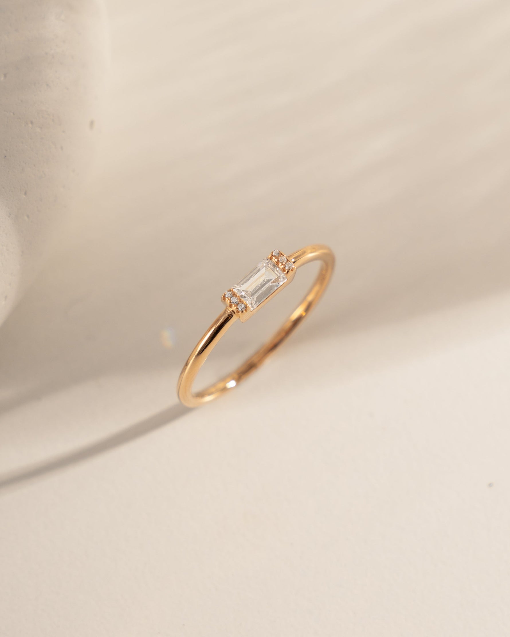 Gold ring with a small baguette diamond on a beige stone surface
