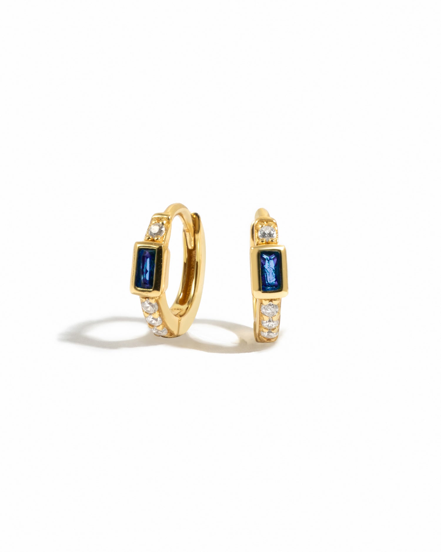 Gold hoop earrings with sapphire gemstones and white cz stones on a white background