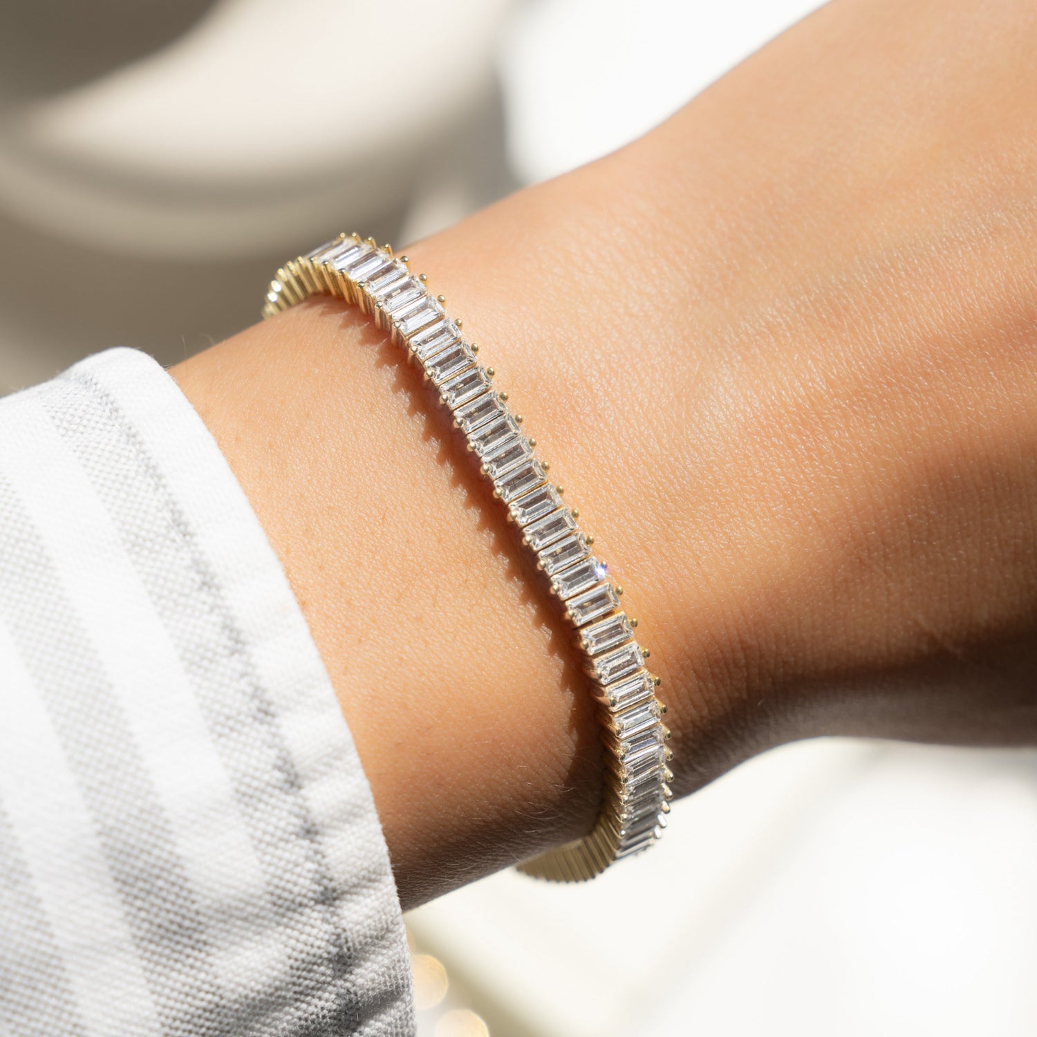 Model wearing gold tennis bracelet with baguette diamonds 