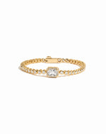 Gold tennis bracelet with a central baguette diamond on a white background