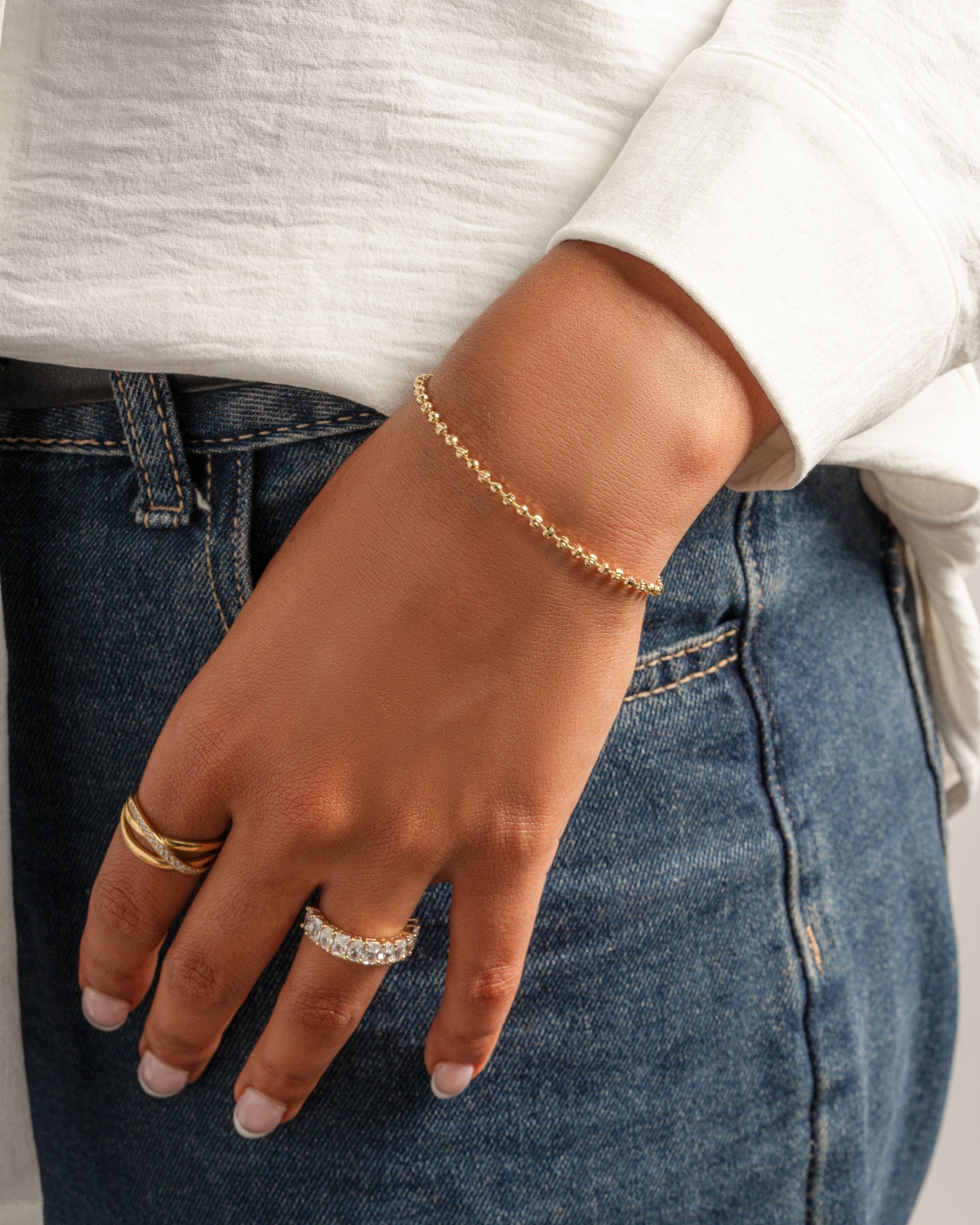 Model wearing gold jewelry featuring a gold beaded chain bracelet and gold stackable rings