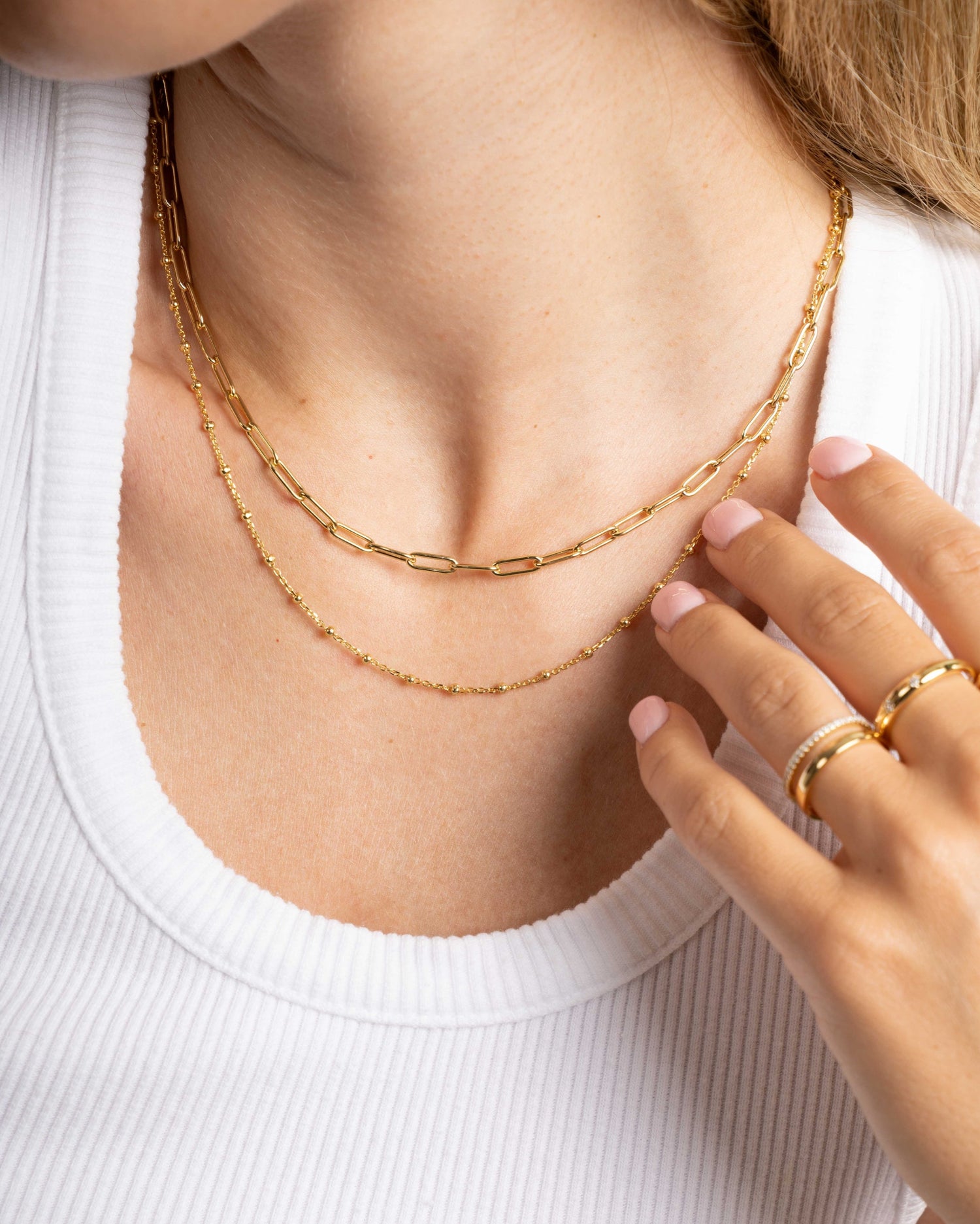 Close-up of a model wearing gold layering necklaces and gold stacking rings 
