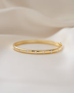 Gold diamond bracelet with small cubic zirconia bezel diamonds on a beige background