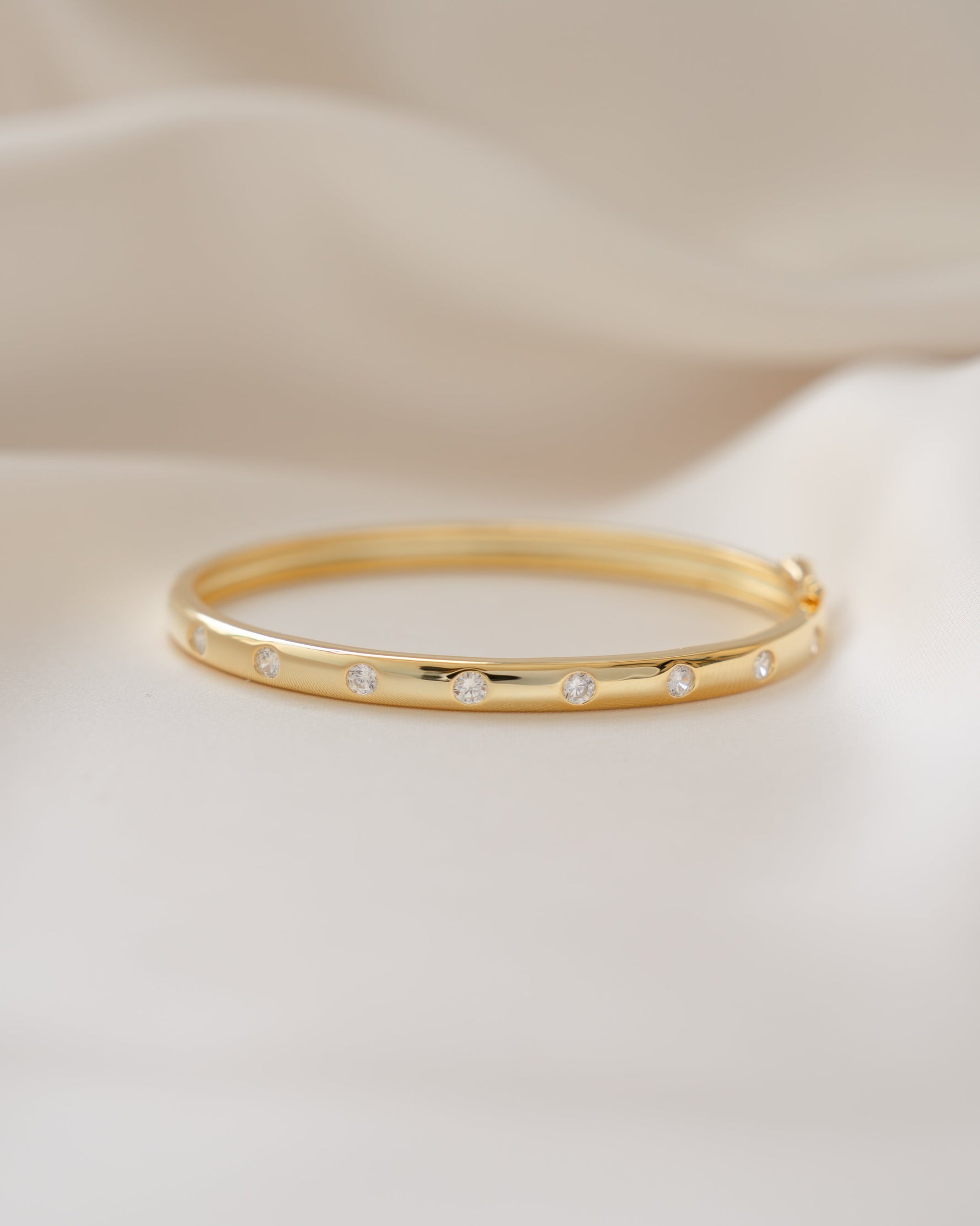 Gold diamond bracelet with small cubic zirconia bezel diamonds on a beige background