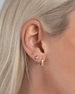 Model wearing bridal jewelry earring stack featuring a gold huggie hoop, a diamond stud earring, and a gold tiny earring