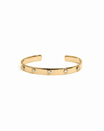 Gold cuff bracelet with small diamonds on a white background