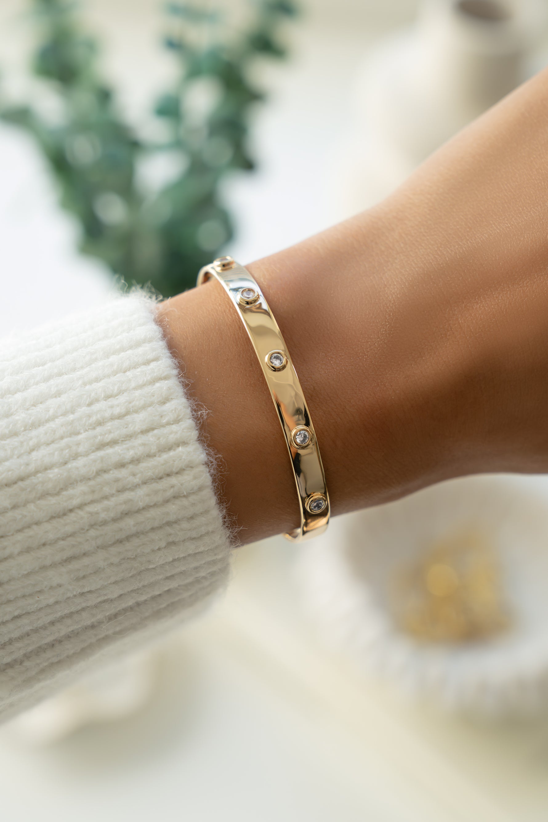 Gold cuff adjustable bracelet on a wrist with a blurred background