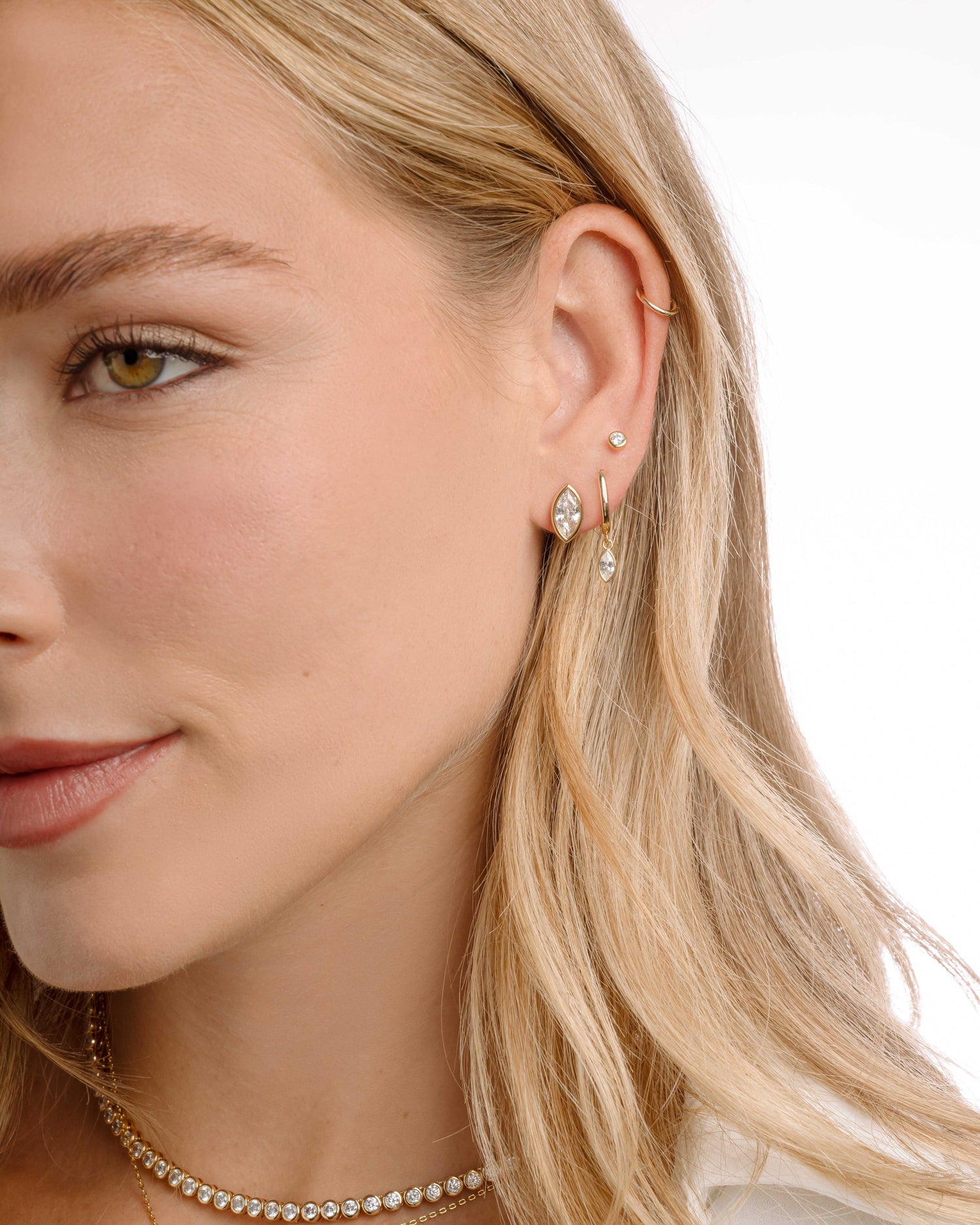 Gold bridal jewelry earring stack featuring a marquise cut cubic zirconia earring, a small gold hoop, and a diamond stud, model is also wearing gold necklaces