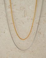 Two gold and silver chain necklaces on a beige textured background