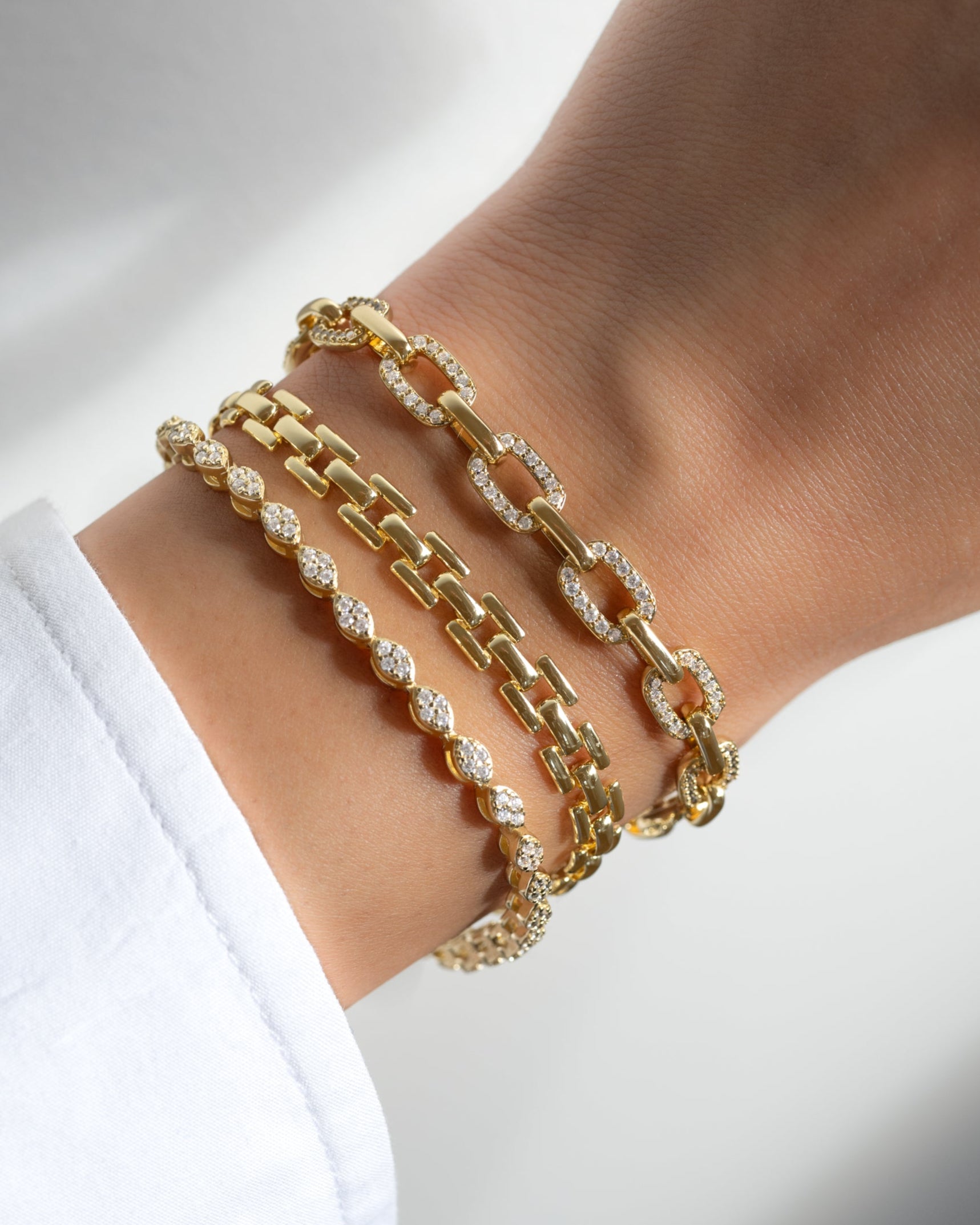 model wearing gold bracelet stack featuring a marquise shaped diamond bracelet, a chain link bracelet and a pave paperclip statement bracelet
