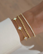 gold stackable bracelets on model with a four leaf clover gold chain bracelet, a twisted chain bracelet, and a classic gold tennis bracelet