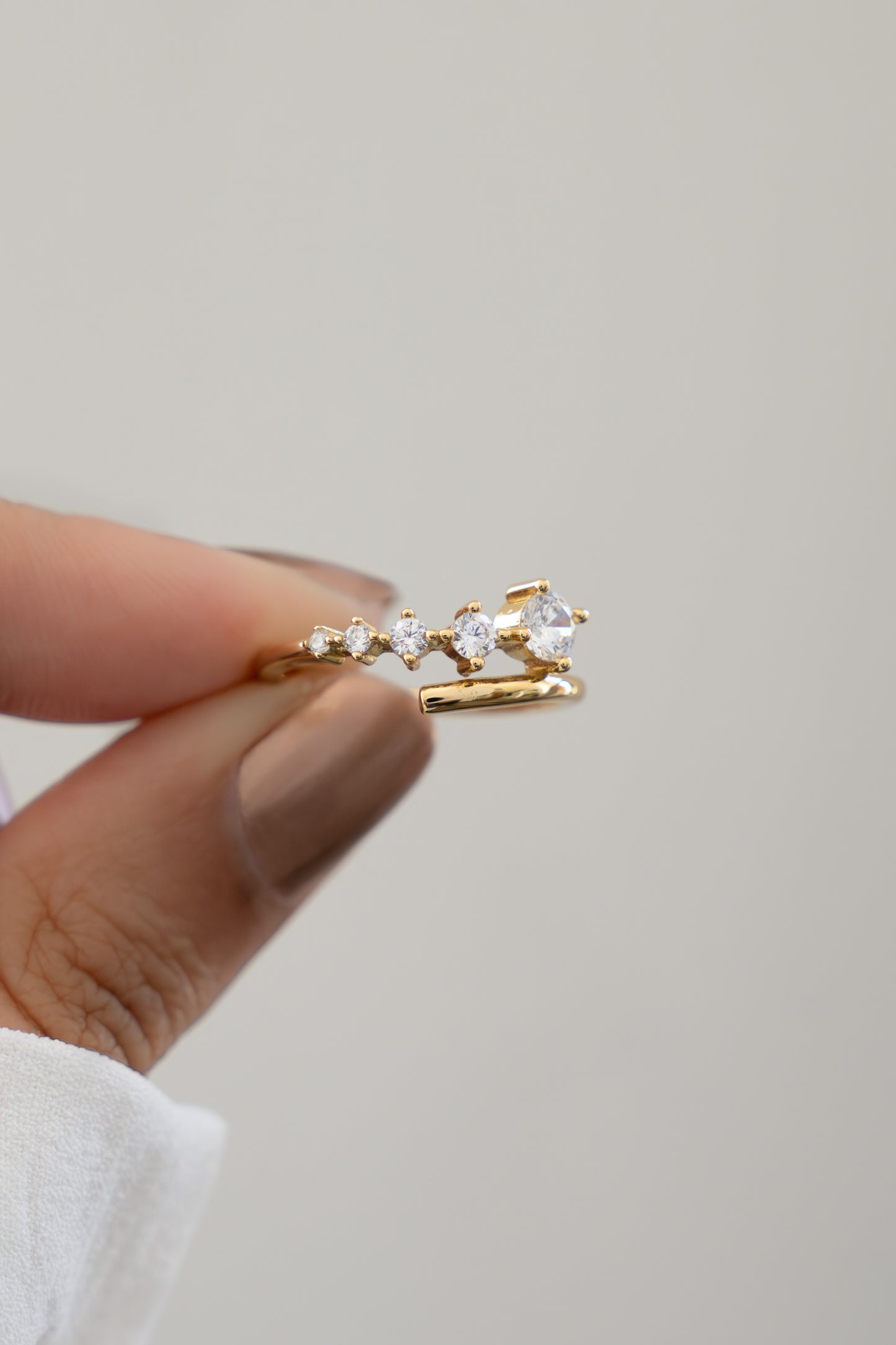 Closeup of hand holding Sami Jewels gold plated bypass spiral ring with 5 CZ diamonds