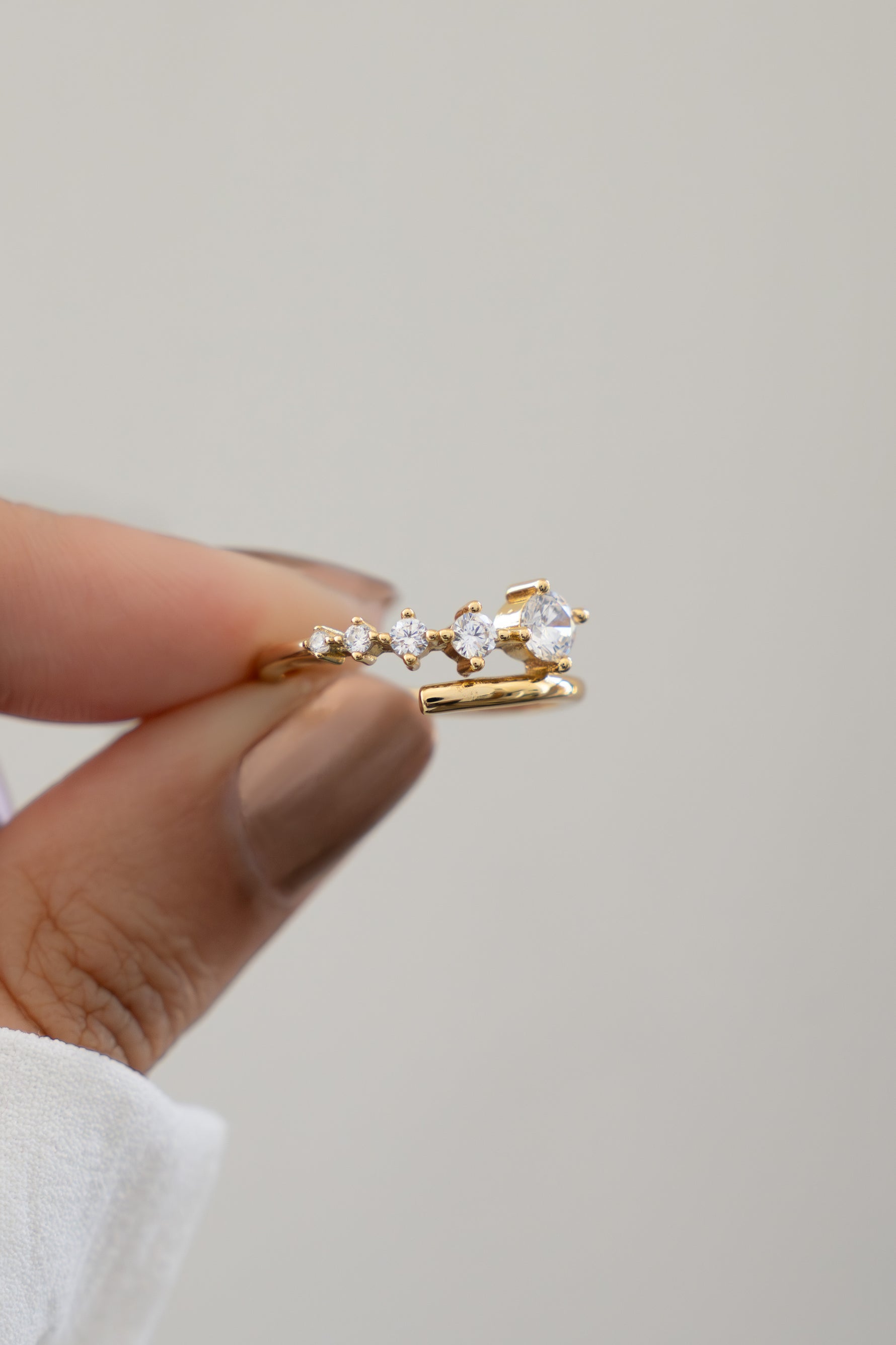 Closeup of hand holding Sami Jewels gold plated bypass spiral ring with 5 CZ diamonds