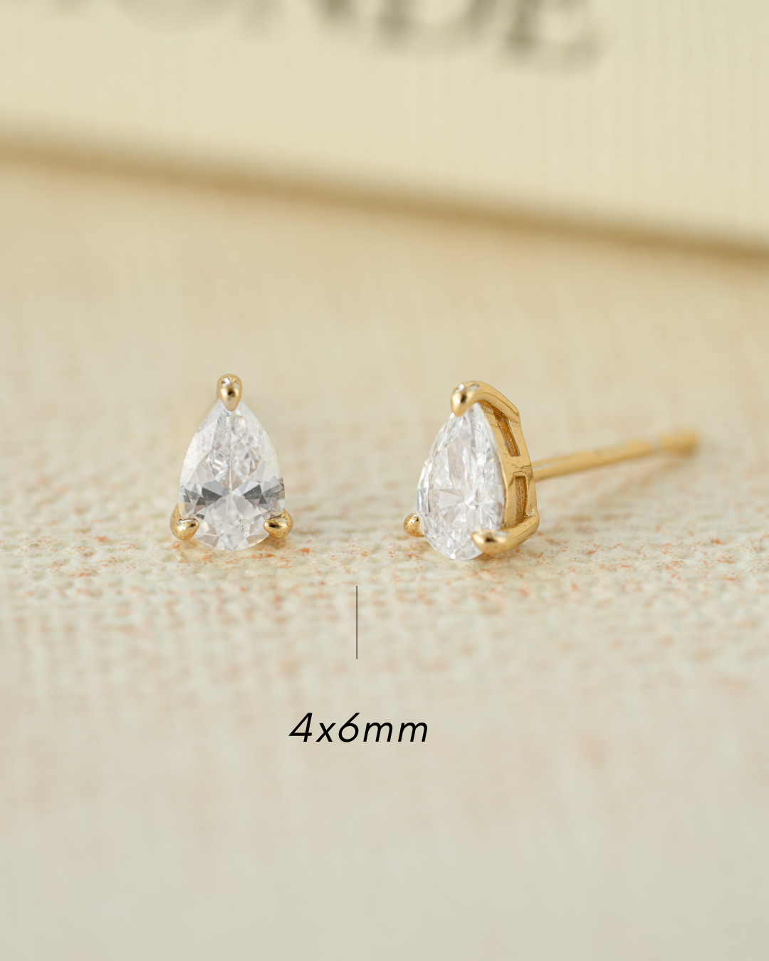 Gold teardrop-shaped stud earring on a light beige background