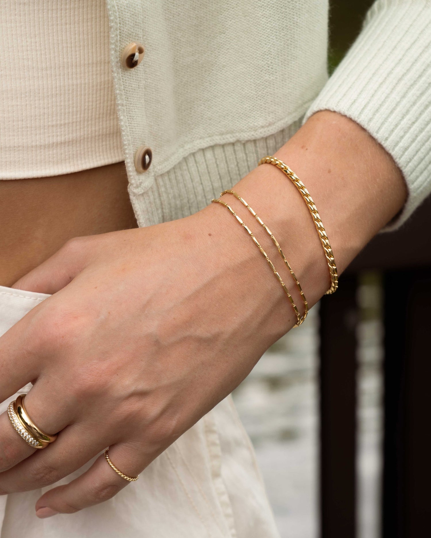 Model wearing gold chain bracelet stack featuring a gold beaded bracelet set, and a gold chunky bracelet, with two gold rings, one statement ring and one stackable ring