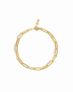 A gold-colored paperclip chain bracelet with a lobster clasp closure, displayed on a marble surface.