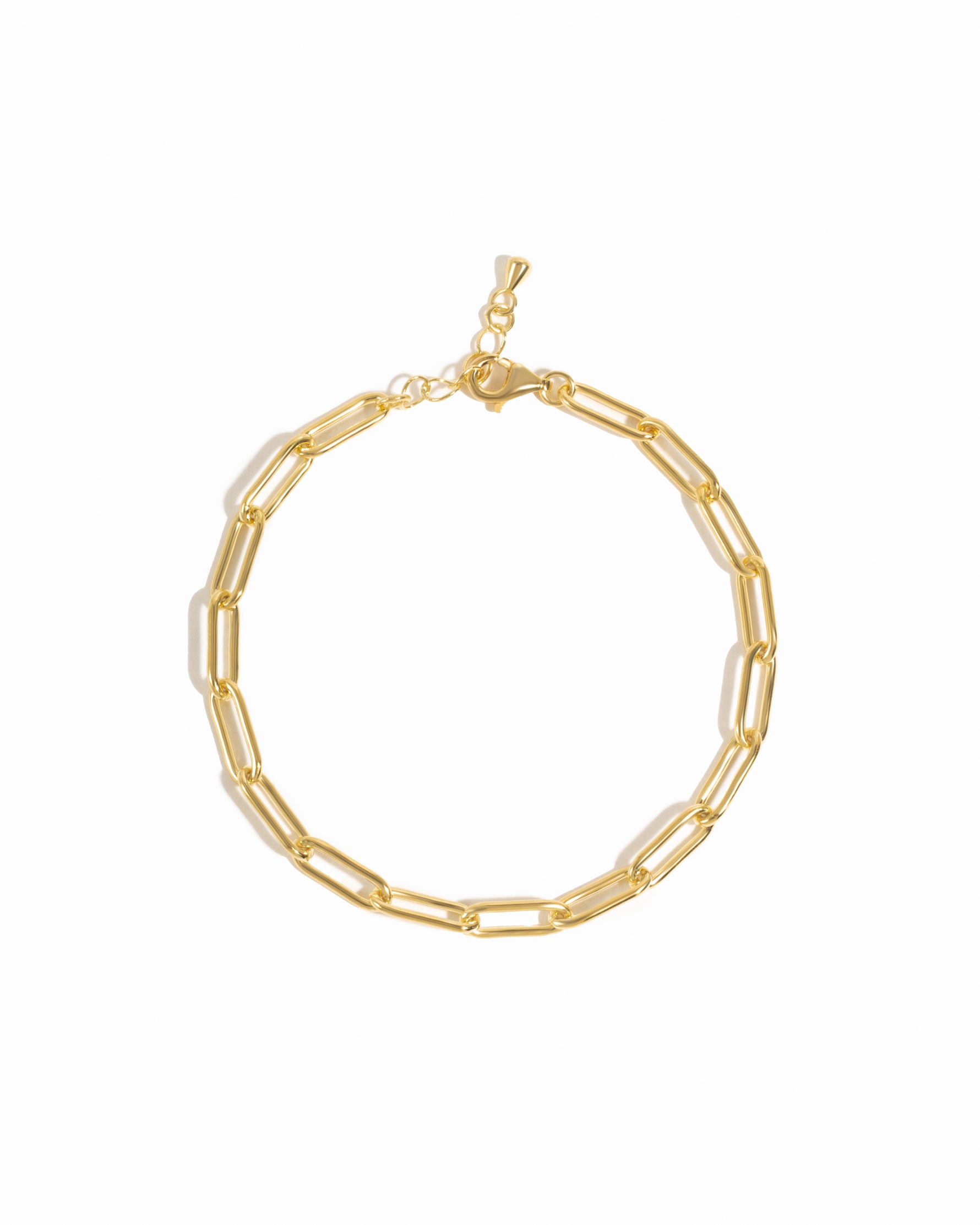 A gold-colored paperclip chain bracelet with a lobster clasp closure, displayed on a marble surface.