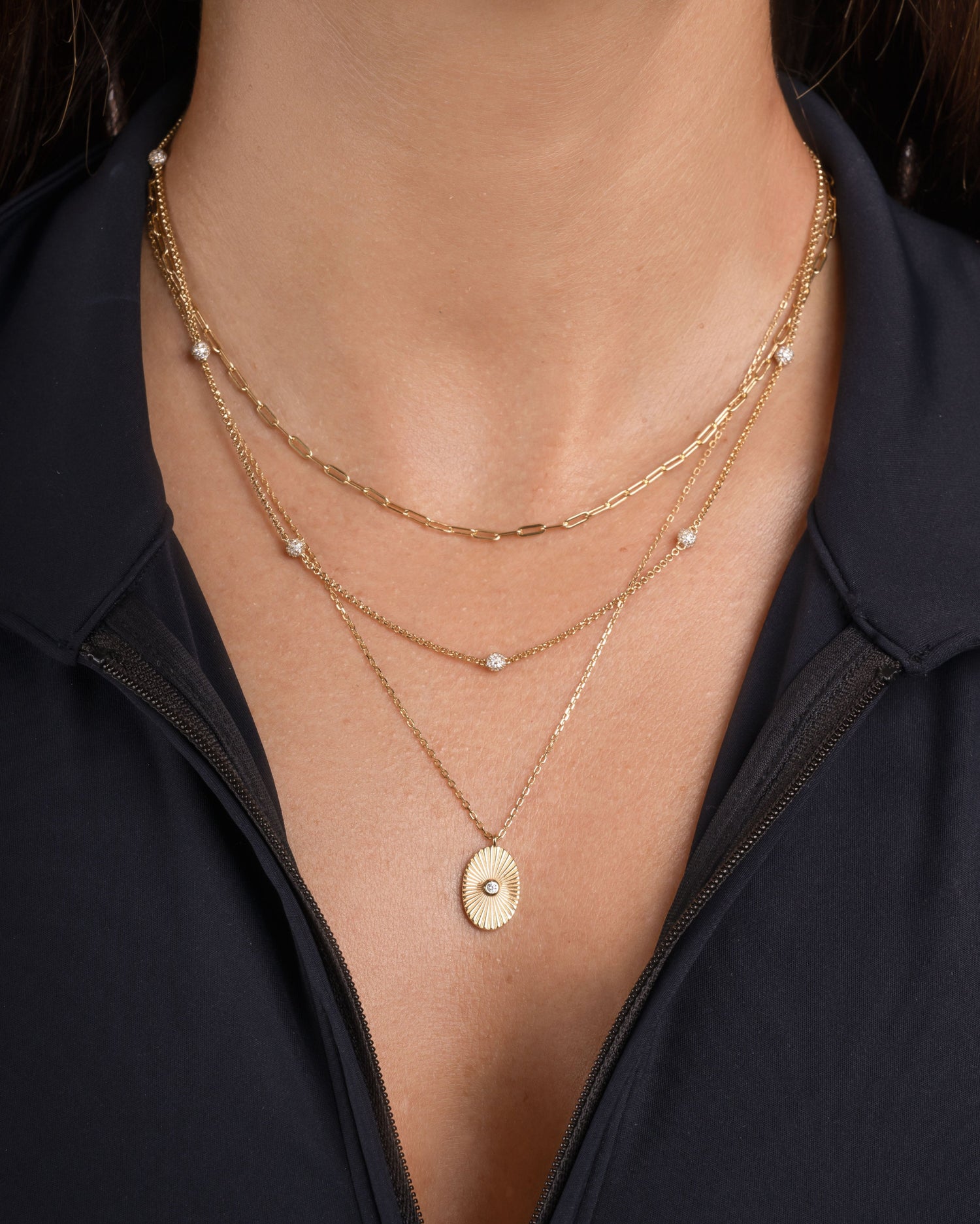 Model wearing layering necklaces, featuring a oval pendant necklace, a beaded diamond necklace, and a tiny paperclip chain necklace