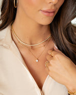 Close-up of a model wearing gold jewelry featuring a diamond tennis necklace, a diamond pendant necklace a simple gold chain necklace, and gold stackable rings