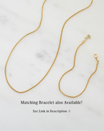 Gold chain necklace on a marble surface with text about a matching bracelet.