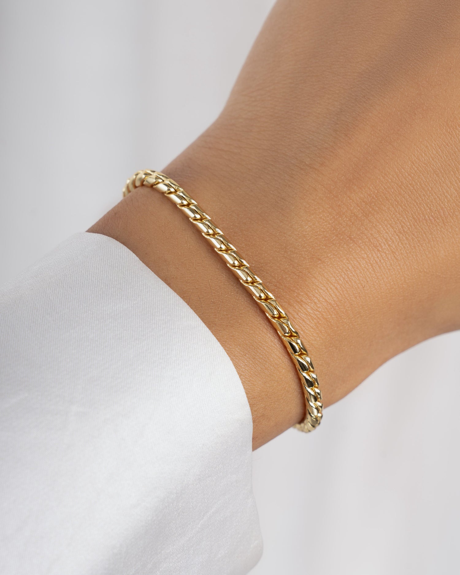 Gold chain statement bracelet on a wrist with a white background