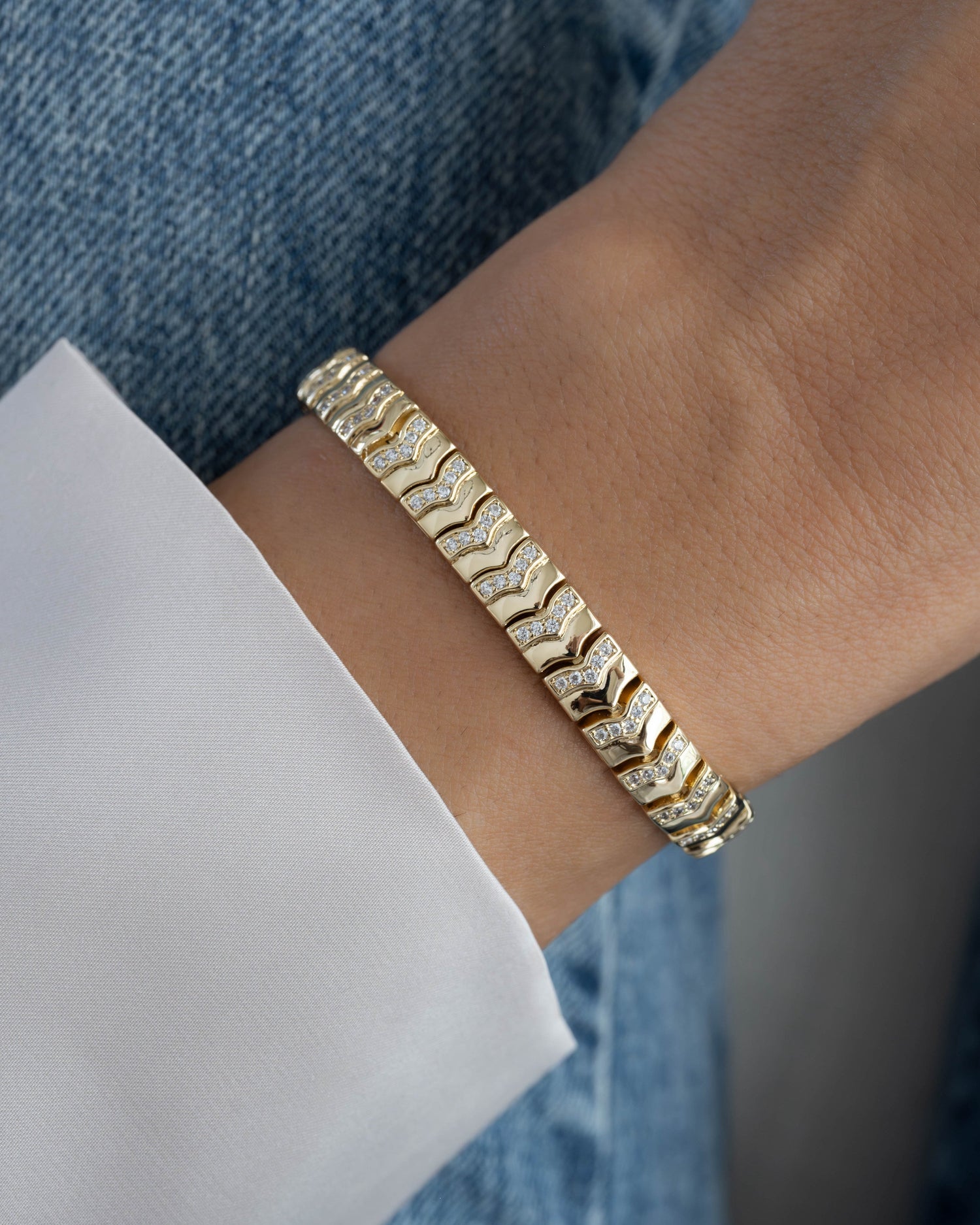Gold tennis bracelet with cubic zirconia stones and a chevron pattern on a models wrist