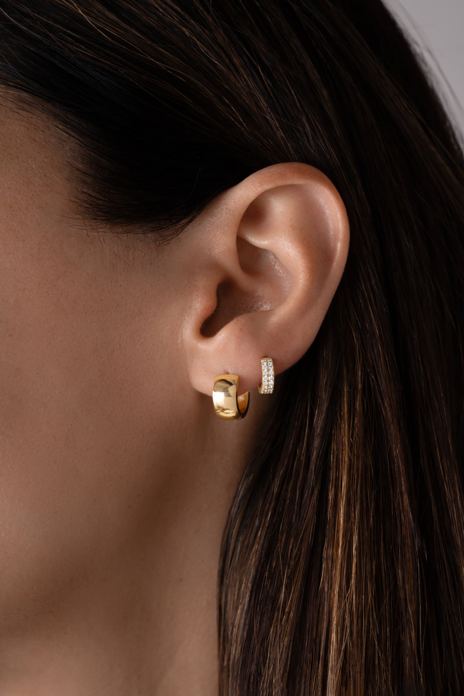 Model wearing gold chunky hoop earrings and two row diamond huggie earring 