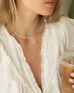 Model wearing gold layering necklaces featuring a simple diamond tennis necklace, a diamond beaded necklace and a gold cross necklace
