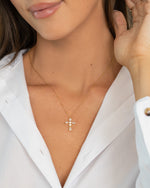 Close-up of a model wearing a dainty gold cross necklace with a white shirt.