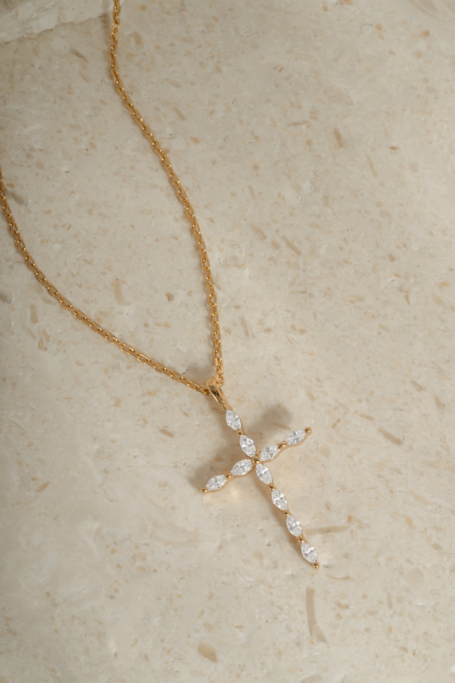 Gold chain dainty necklace with a diamond cross pendant on a beige background