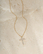 Gold gemstone necklace with a cross pendant on a beige stone surface