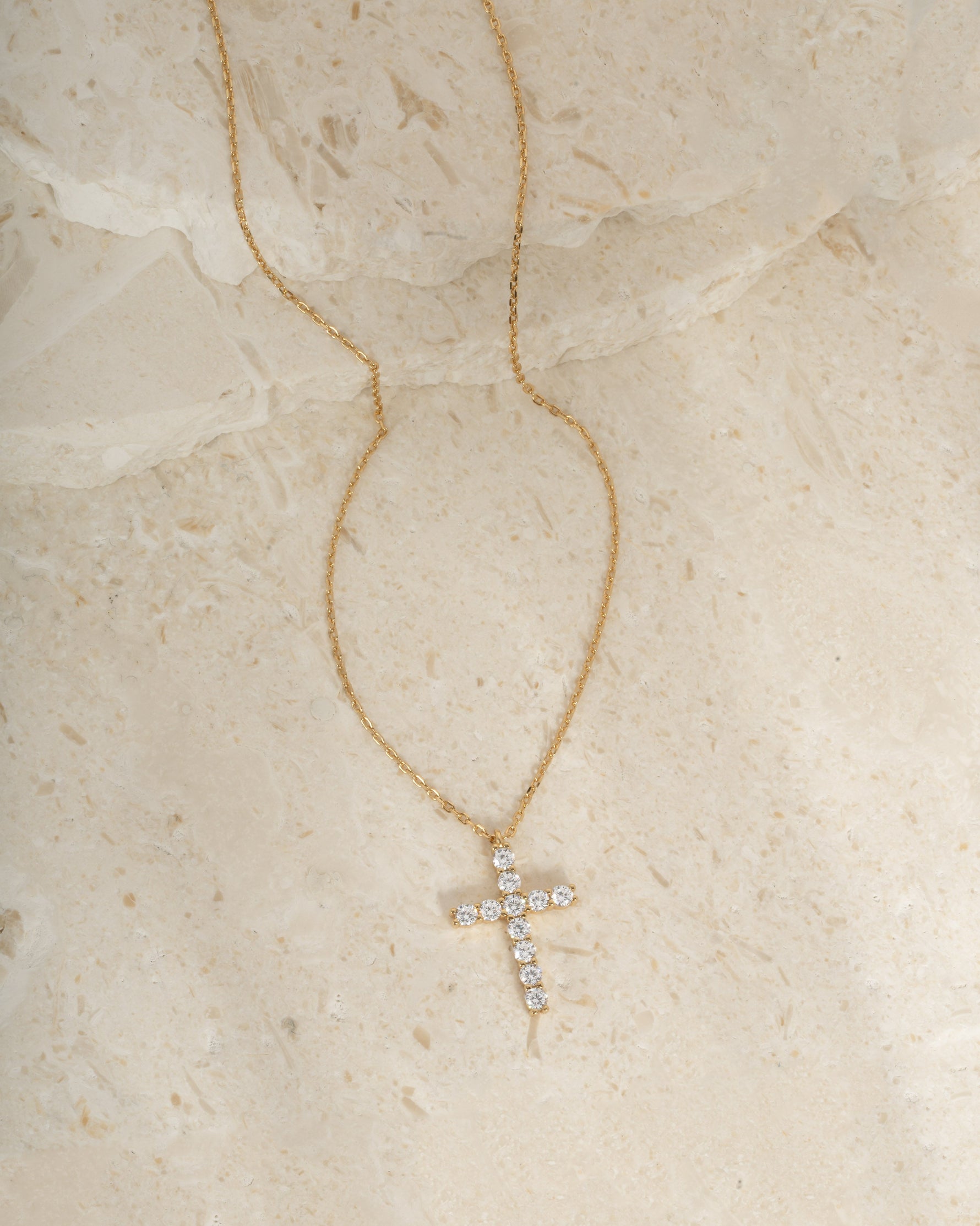 Gold gemstone necklace with a cross pendant on a beige stone surface