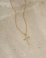 Gold gemstone necklace with a diamond cross pendant on a beige background