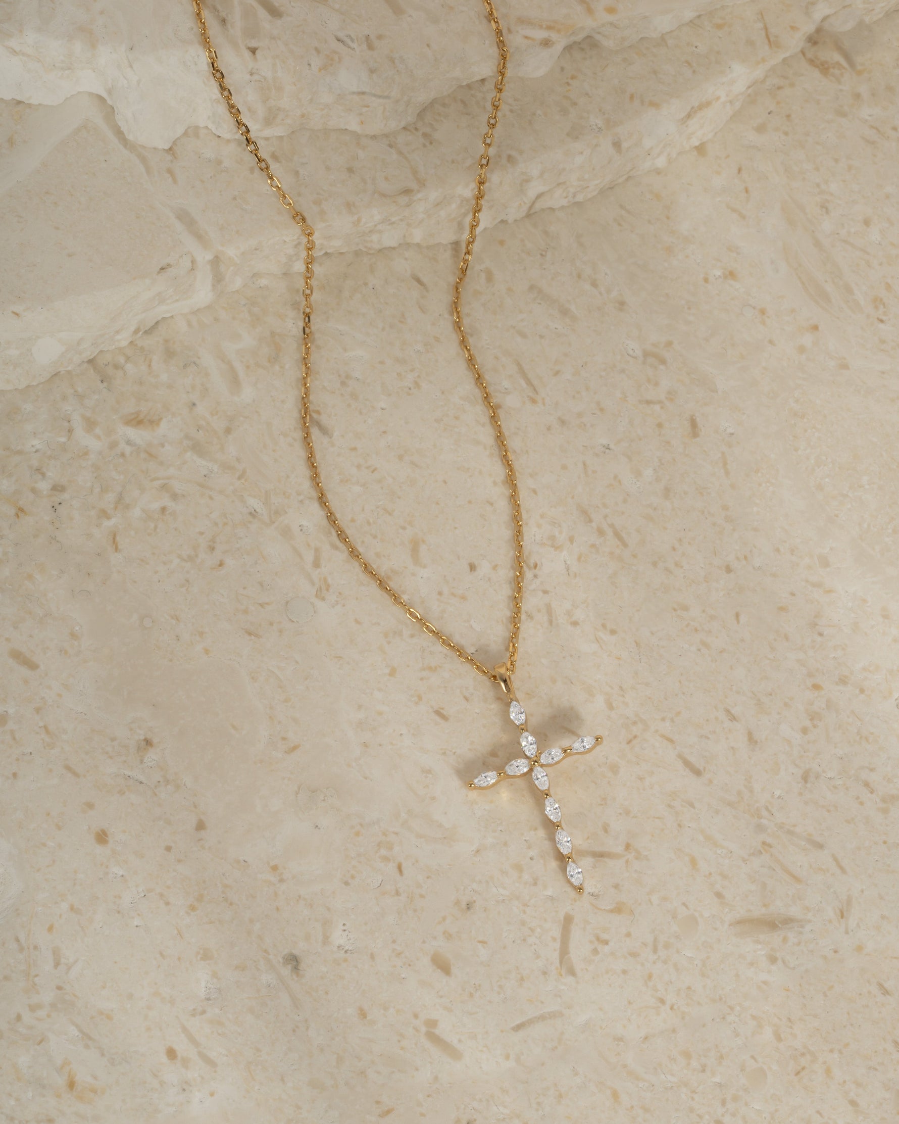 Gold gemstone necklace with a diamond cross pendant on a beige background