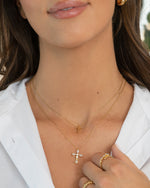 Gold layering necklaces on model featuring a simple dainty cross necklace and a diamond pendant cross necklace, with gold stackable rings