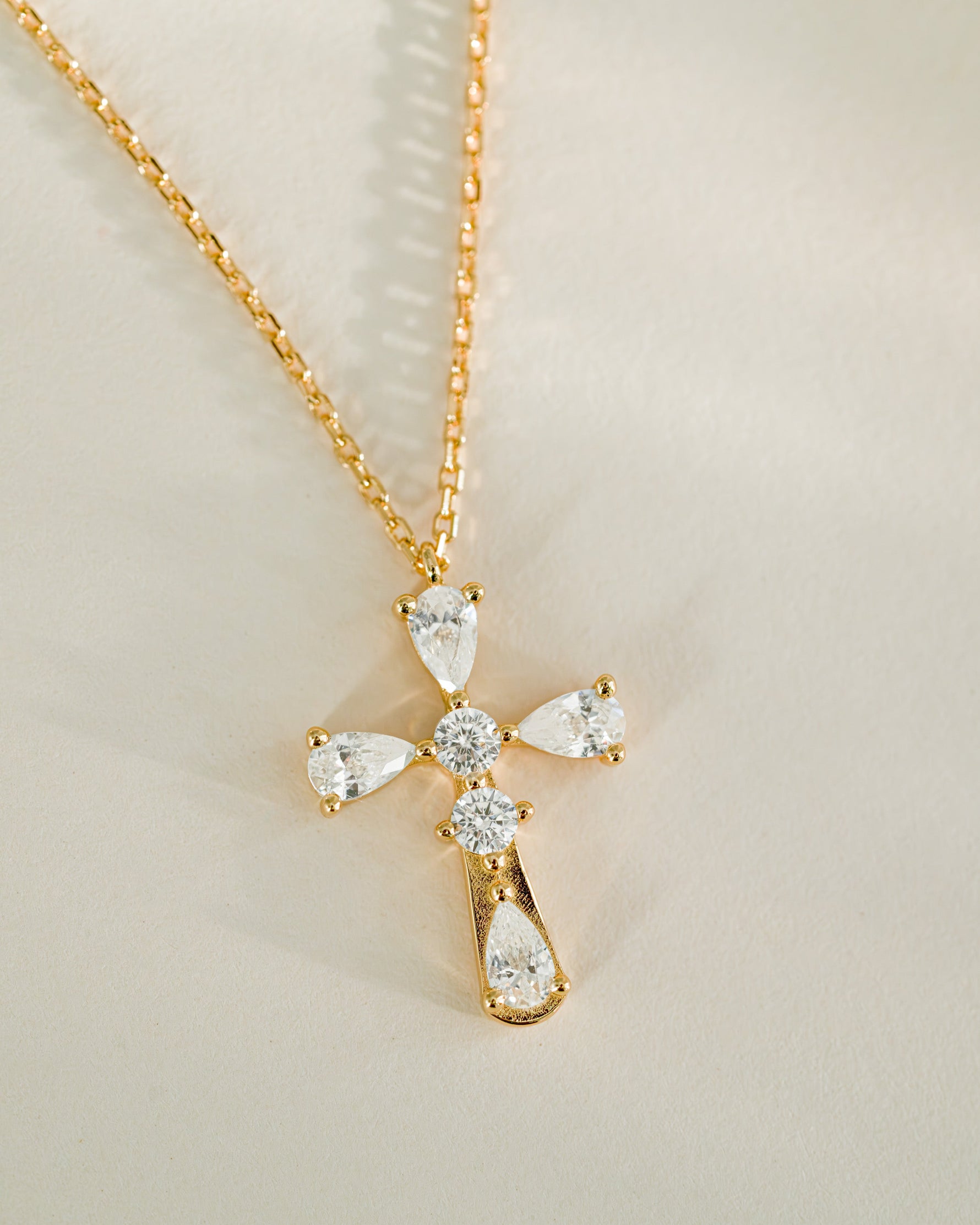 Gold cross necklace with teardrop-shaped gemstones on a light background